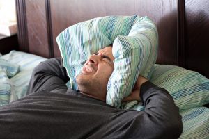 a man having trouble sleeping squeezes a pillow around his ears for some peace and quiet_Ht0bpVdASo1 300x200